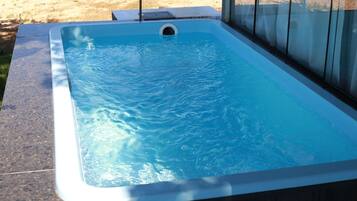 Uma banheira de hidromassagem retangular com interior azul transparente, rodeada por um deck revestido com azulejos.