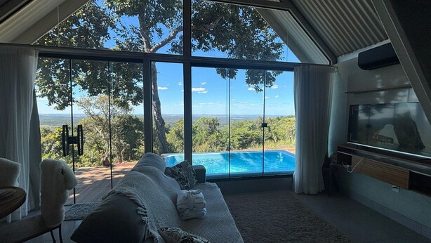 Ein modernes Wohnzimmer mit einem großen Fenster mit Blick auf einen Pool und üppige Vegetation.