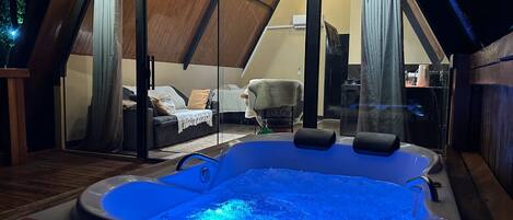 A hot tub in a room with a sloped ceiling and a glass door leading to a bedroom.