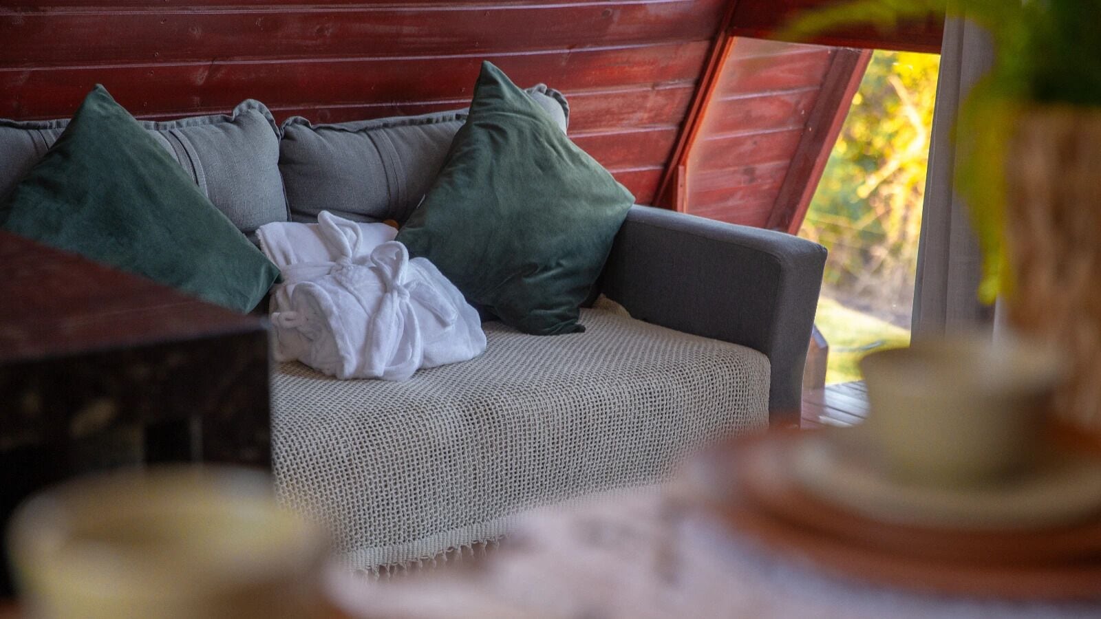 Interior acolhedor de uma cabana com sofá de palha, almofadas e parede de madeira rústica.