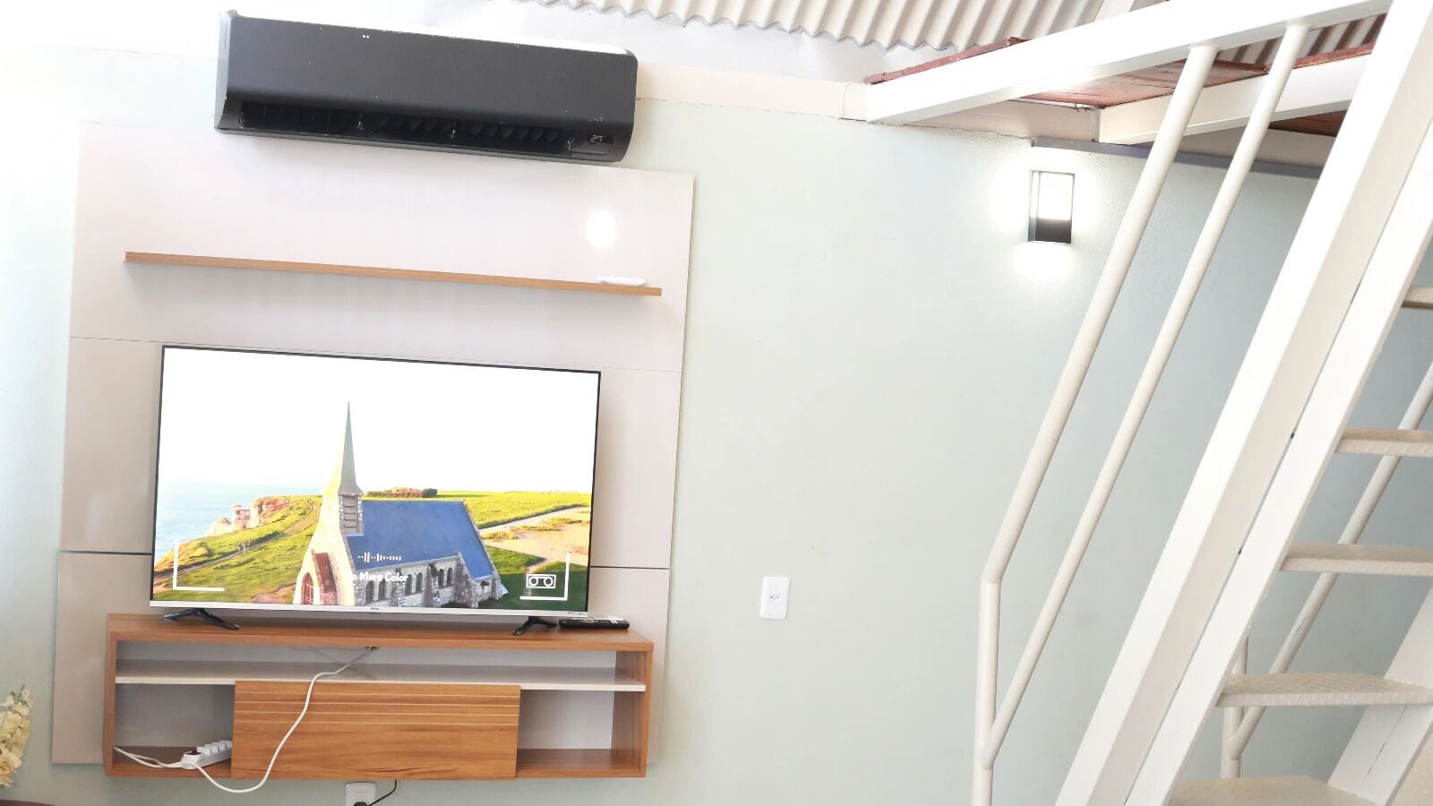 Un téléviseur à écran plat fixé au mur, avec une étagère en bois en dessous.