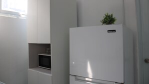A kitchen with a white refrigerator, a microwave, and a small shelf.