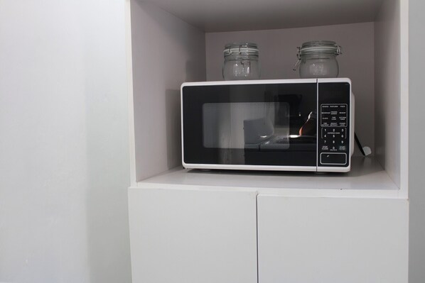 Un horno microondas sobre un estante blanco con dos frascos de vidrio encima.