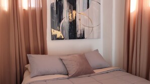 A hotel room with a bed, beige curtains, and a painting on the wall.