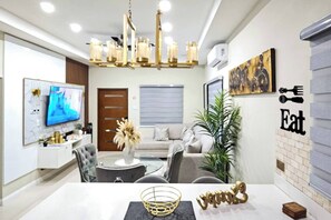 Una sala moderna con televisión, sofá, mesa de comedor y elementos decorativos.