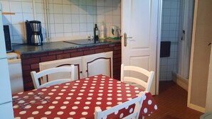 Una cocina con mantel rojo de lunares, sillas blancas y una cafetera sobre la encimera.