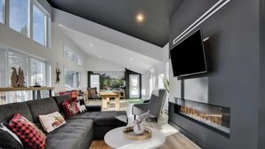 A modern living room with a fireplace, a flat-screen TV, and a dining area visible through an open door.