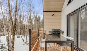 Ein moderner Essbereich im Freien mit einer Holzterrasse, einem Glastisch und weißen Stühlen.