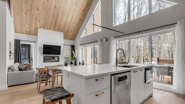 A modern kitchen with a large island, wooden ceiling, and large windows.
