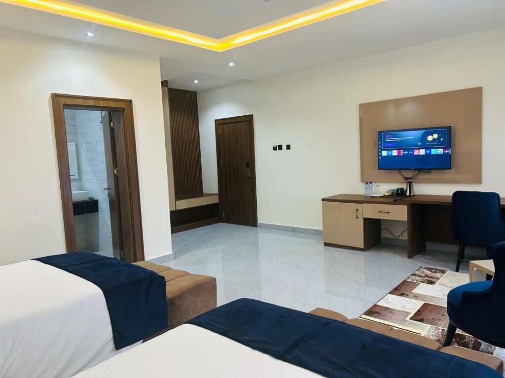 A modern hotel room with a bed, a desk, a chair, a television, and a small table.