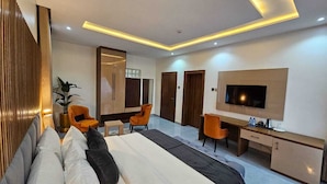 Una habitación de hotel moderna con una cama grande, dos sillones naranjas, un escritorio, un televisor y un armario.