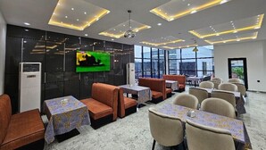 Un comedor moderno con cabinas y mesas, un televisor de pantalla plana en la pared y ventanas amplias con vista a la ciudad.