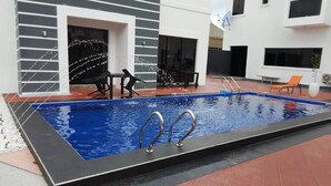 Una piscina rectangular con escaleras metálicas, rodeada por una terraza con baldosas rojas y grises.