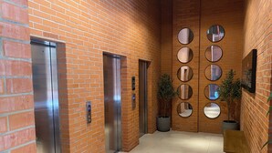 Un pasillo con dos ascensores, una planta en maceta y un muro con espejos circulares.