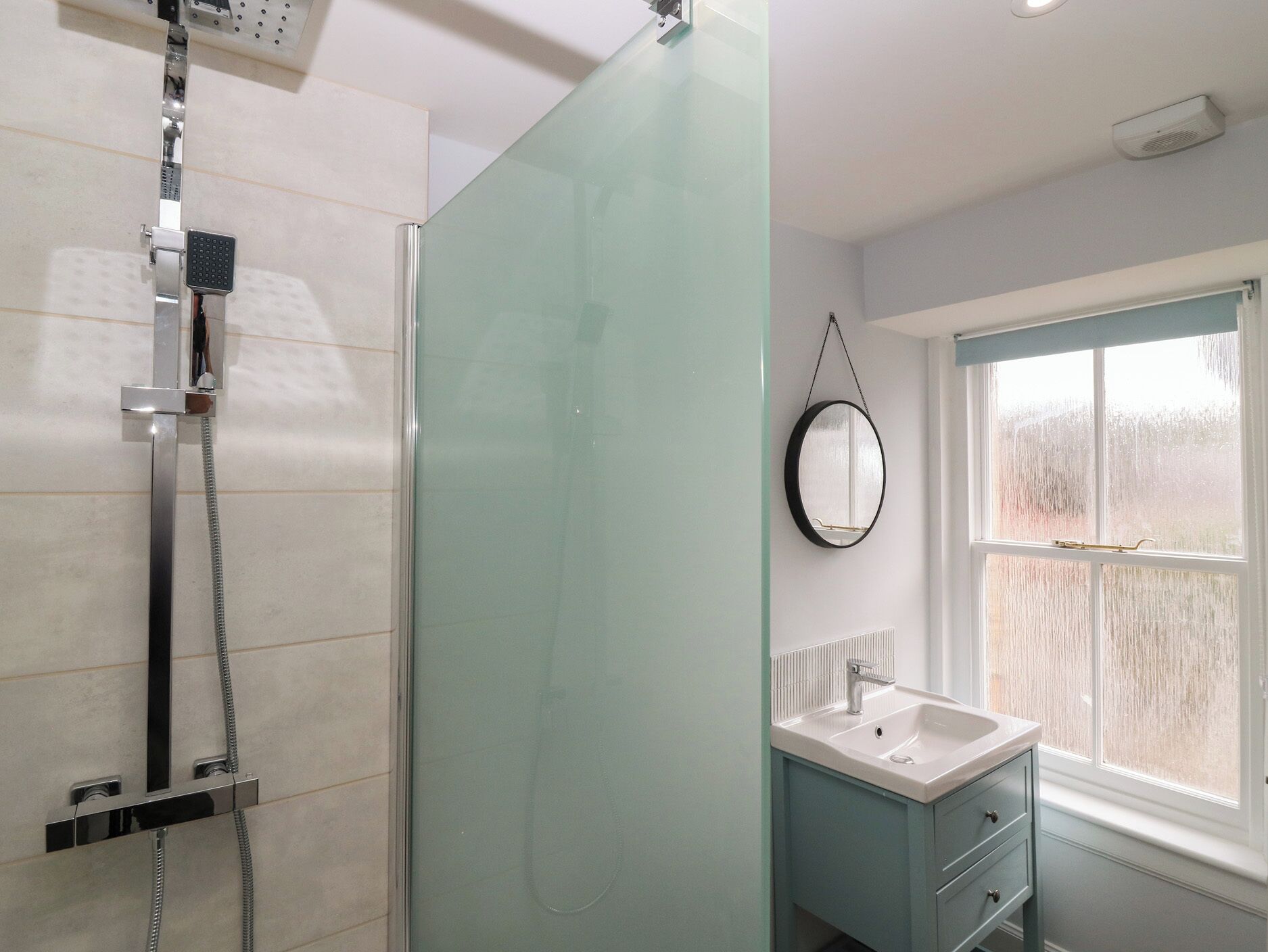 Un baño con cabina de ducha de vidrio, un lavabo con espejo y una ventana con vistas a árboles.