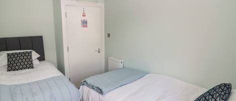 Un dormitorio con dos camas, una puerta blanca con un letrero y una lámpara en el techo.