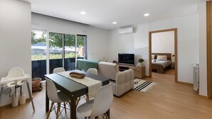 A modern apartment with a dining area, a living room with a TV, a bedroom, and a large window.