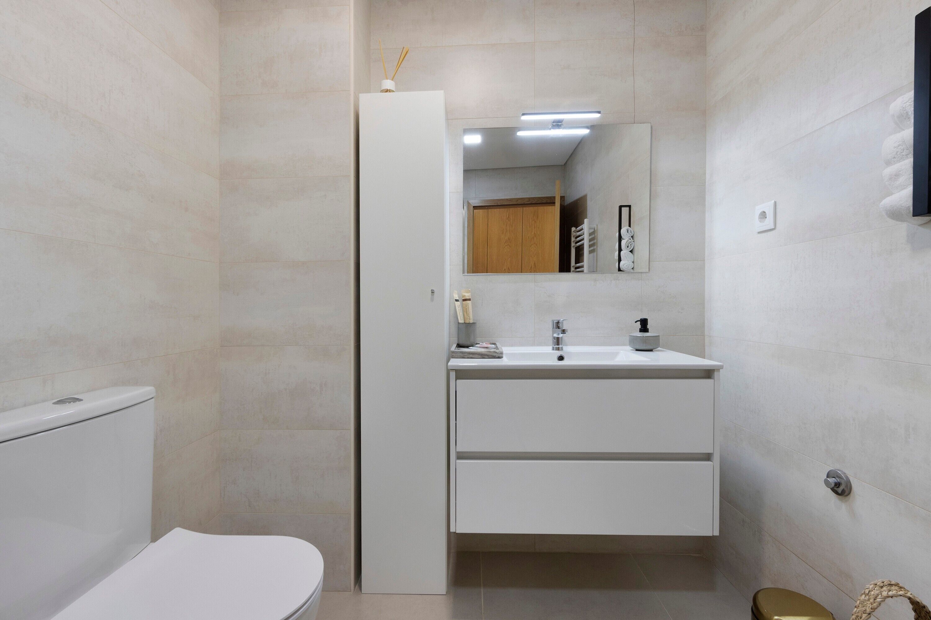 A modern bathroom with a toilet, a sink with a mirror above it, and a towel rack on the wall.