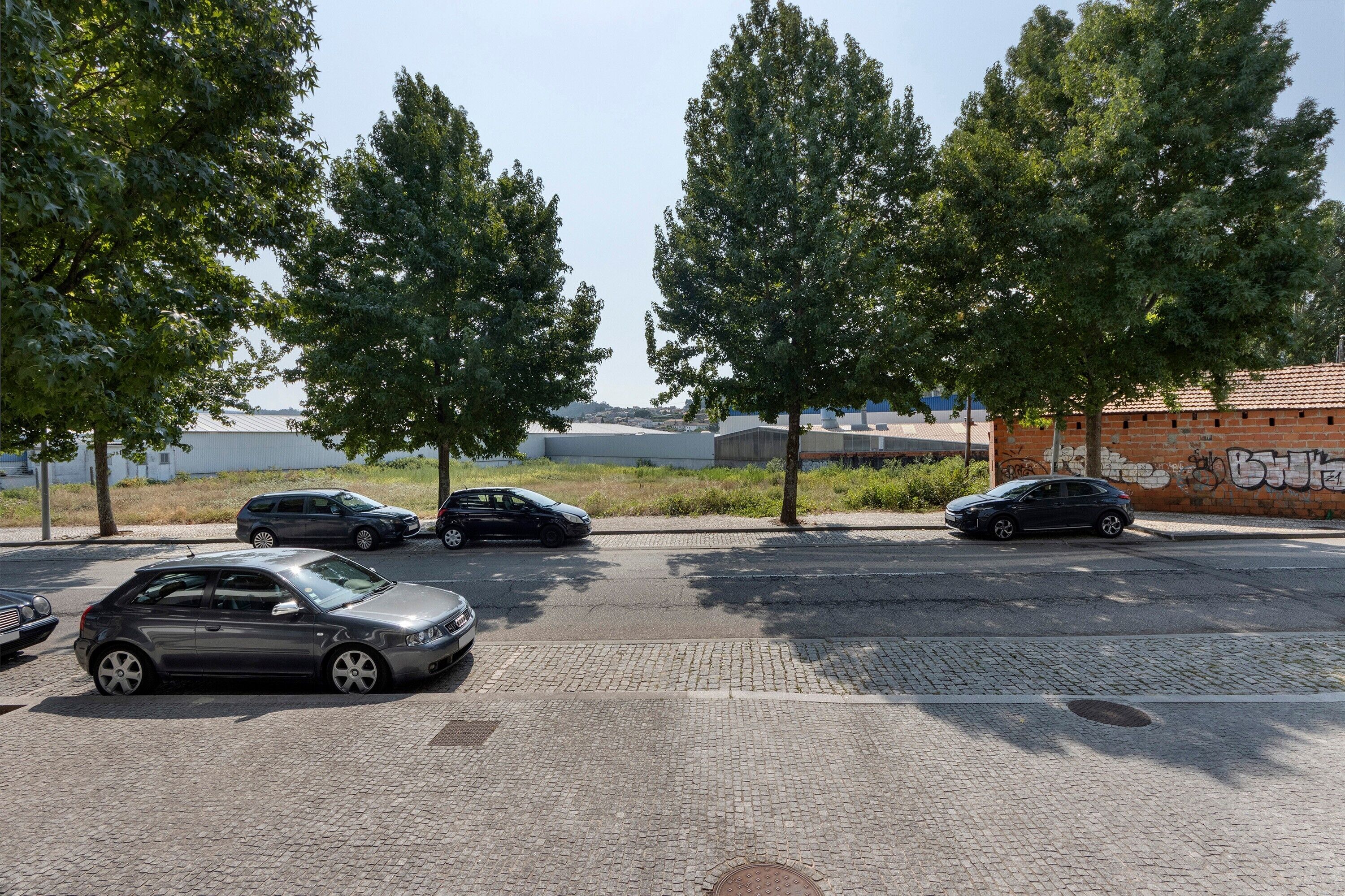 A parking lot with cars, trees, and a building with graffiti.
