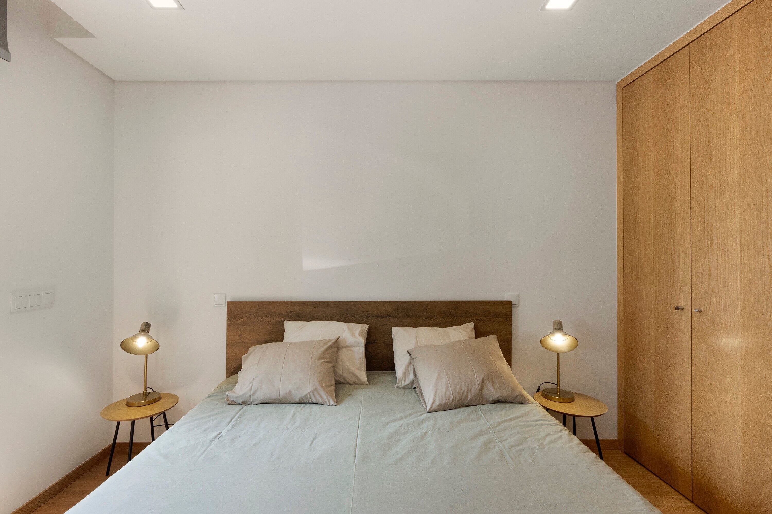 A bedroom with a bed, two bedside lamps, a wooden wardrobe, and a round table.