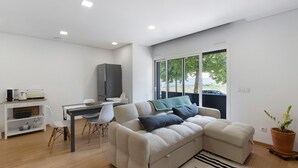 A modern living room with a sofa, a dining table, a TV, and a window with a view.