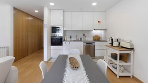 A modern kitchen with white cabinets, a wooden door, a microwave, an oven, a coffee maker, and a toaster on a wooden table.