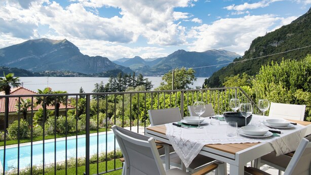 A dining table set on a balcony with a view of mountains and a lake. - Hidden Gem-Villa with private pool Bellagio view (Lierna)