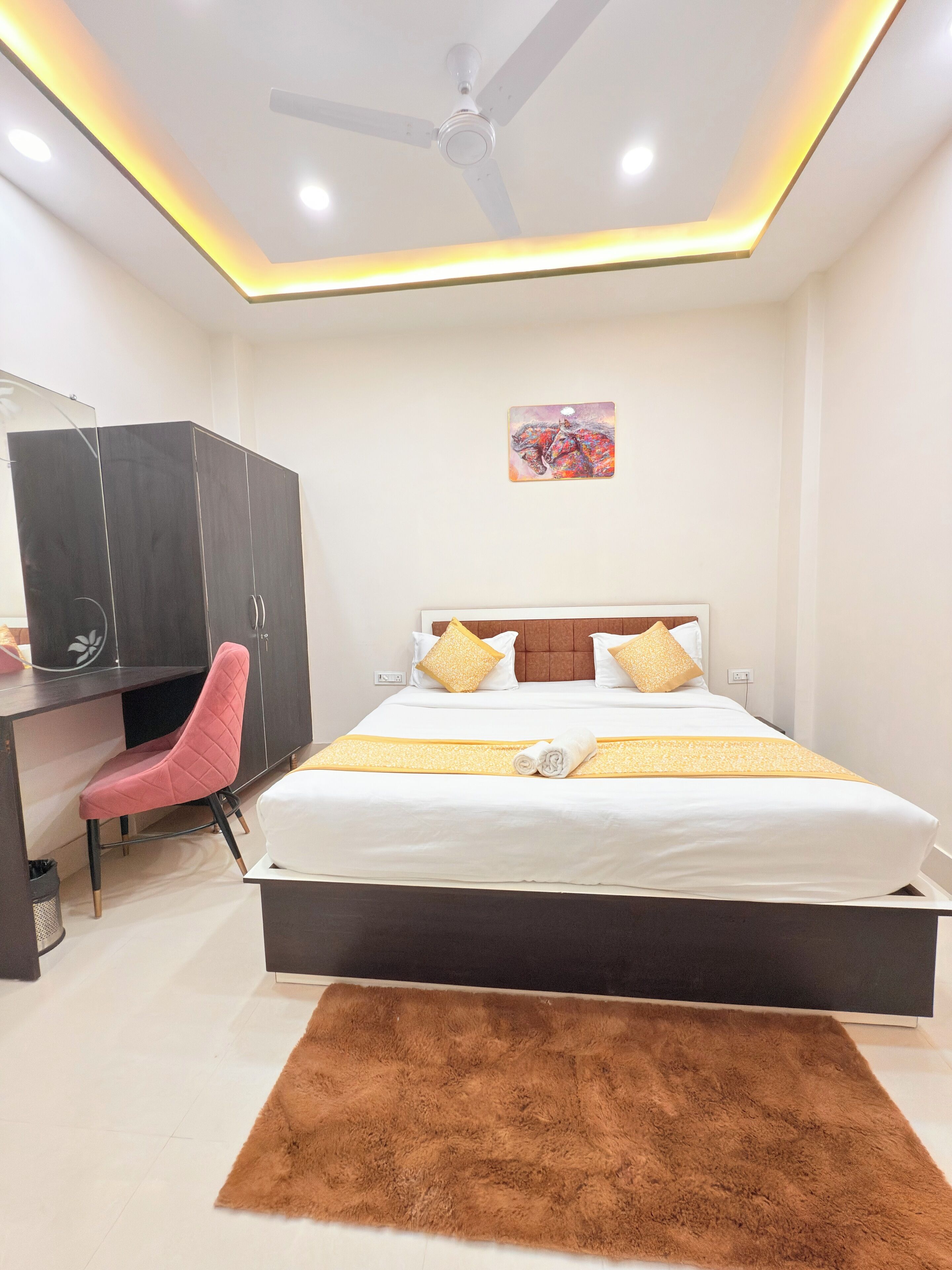 Quarto de hotel com cama, escrivaninha, cadeira, ventoinha no teto e tapete.