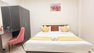 Quarto de hotel com cama, escrivaninha, cadeira, ventoinha no teto e tapete.