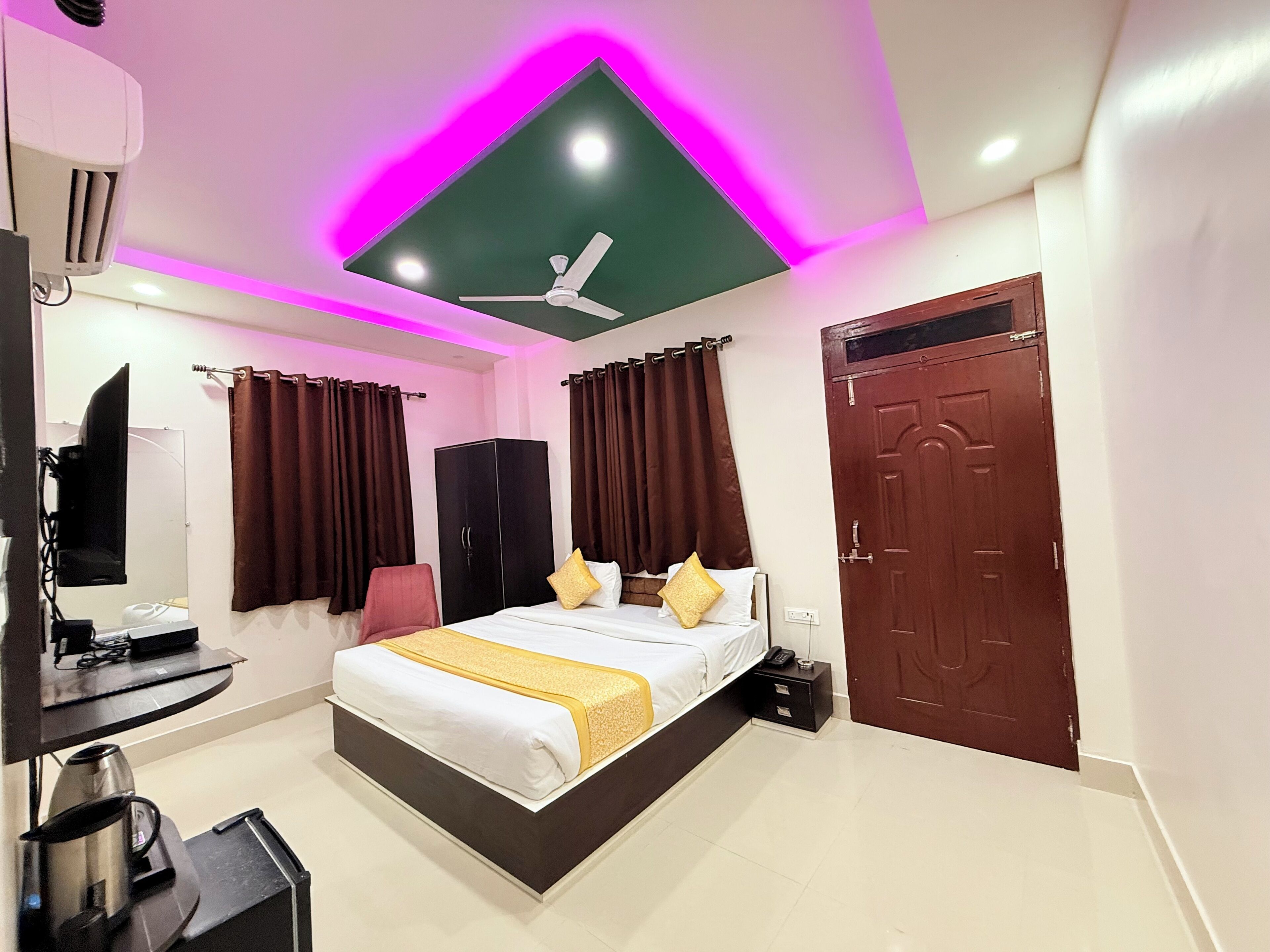 A modern hotel room with a bed, a desk with a computer, a chair, a wardrobe, and a door.