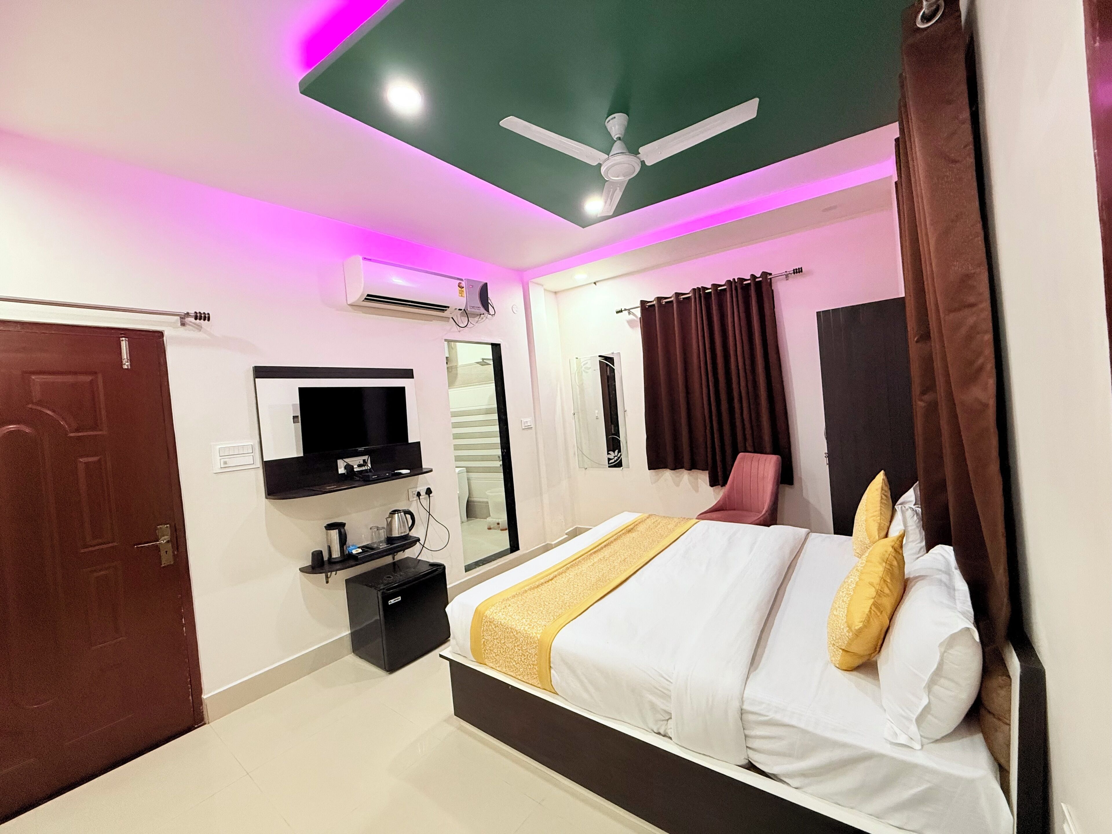 Une chambre moderne équipée d’un lit, d’une télévision, d’un ventilateur de plafond et d’une petite table avec une bouilloire.