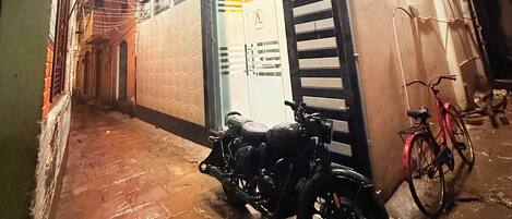 Une ruelle étroite où est garée une moto, devant un immeuble aux fenêtres grillagées et sur lequel on peut voir une enseigne indiquant qu’il s’agit d’un hôtel.