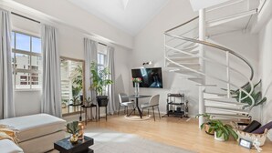 A modern living room with a spiral staircase, a flat-screen TV, and a dining area with a round table. - 104 Hideaway Loft Studio (Cape Town)