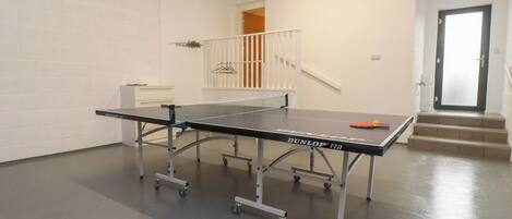 A ping pong table in a room with white walls, a staircase, and a door.