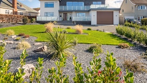 Une maison moderne à deux étages, dotée d’une grande pelouse à l’avant, d’un garage et d’une allée.