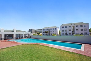 A modern residential building with a swimming pool, flat roof, and a well-maintained lawn.