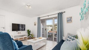Un saló modern amb televisió plana, una taula de cafè blanca, un sofà blau i un balcó amb vistes.