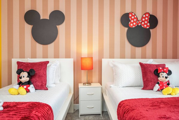 A hotel room with two beds, each with a Mickey Mouse and Minnie Mouse headboard. There is a nightstand with a lamp between the beds. - Cozy 4 BR Decorated Close to Disney W Private Pool (Kissimmee)