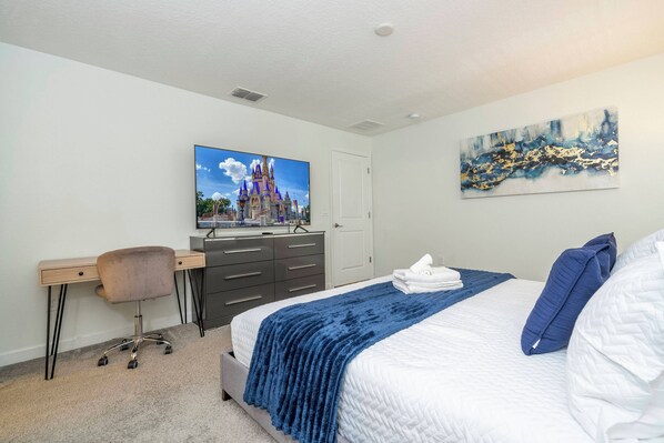 A bedroom with a bed, a desk, a chair, a television, and artwork on the wall.