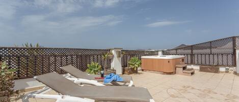 A rooftop terrace with lounge chairs, a hot tub, and potted plants.