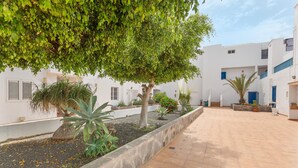 A courtyard with a tree, potted plants, and white buildings with blue doors. - Penthouse with Jacuzzi, Sea & Volcano View (Costa Teguise)