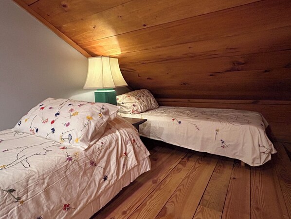 Une petite chambre agréable avec deux lits simples, une table de chevet avec une lampe et des murs en bois.