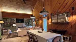 Ein gemütliches Blockhaus-Interieur mit Esstisch, Stühlen, einer Couch und einer Küchenzeile inklusive Fernseher und Regalen.