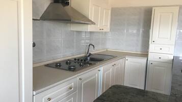 Een koelkast, een oven, een kookplaat, kookgerei, borden en bestek