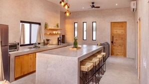A modern kitchen with a central island, bar stools, a ceiling fan, and large windows. - Sun-drenched escape w/ sleek saltwater pool (Todos Santos)