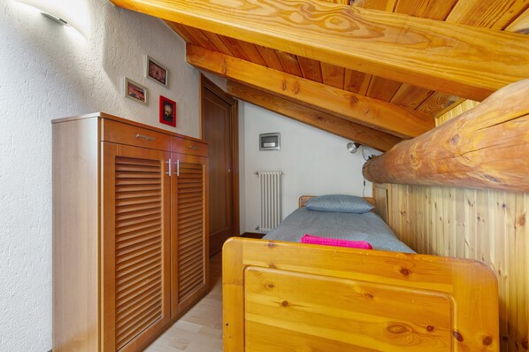 Un dormitorio con cama de madera, armario, radiador y techo con vigas a la vista.