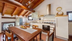 A kitchen with wooden beams, a dining table with chairs, a stove, and a refrigerator. - 'The Traveler’s Attic' Apartment with Mountain View, Private Terrace and Wi-Fi (Pont Saint Martin)
