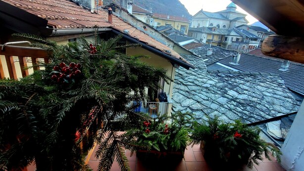 A balcony with potted plants and a view of a town with traditional architecture and a mountain backdrop. - 'The Traveler’s Attic' Apartment with Mountain View, Private Terrace and Wi-Fi (Pont Saint Martin)