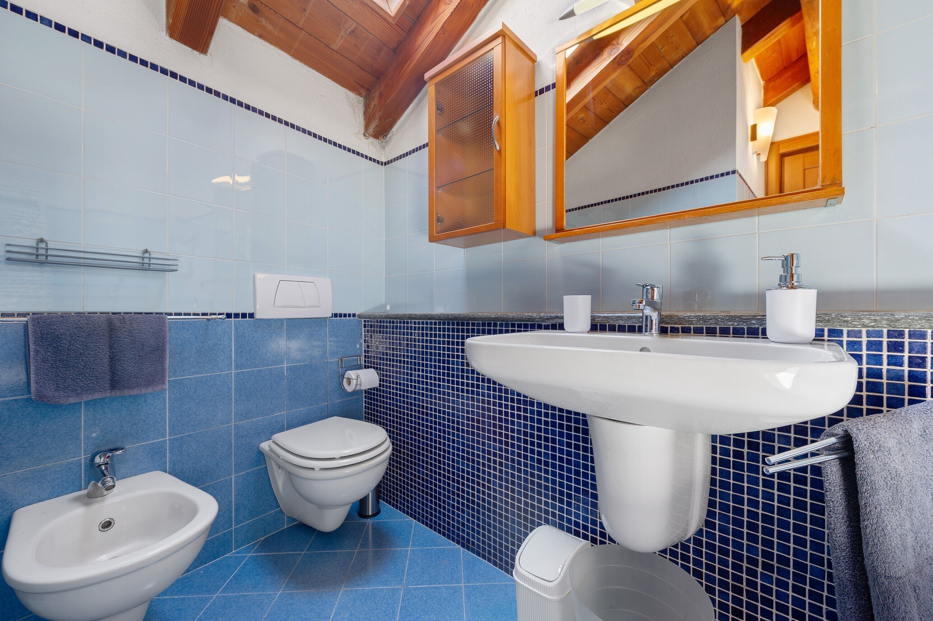 A bathroom with a white sink, a bidet, a toilet, and a mirror above the sink.