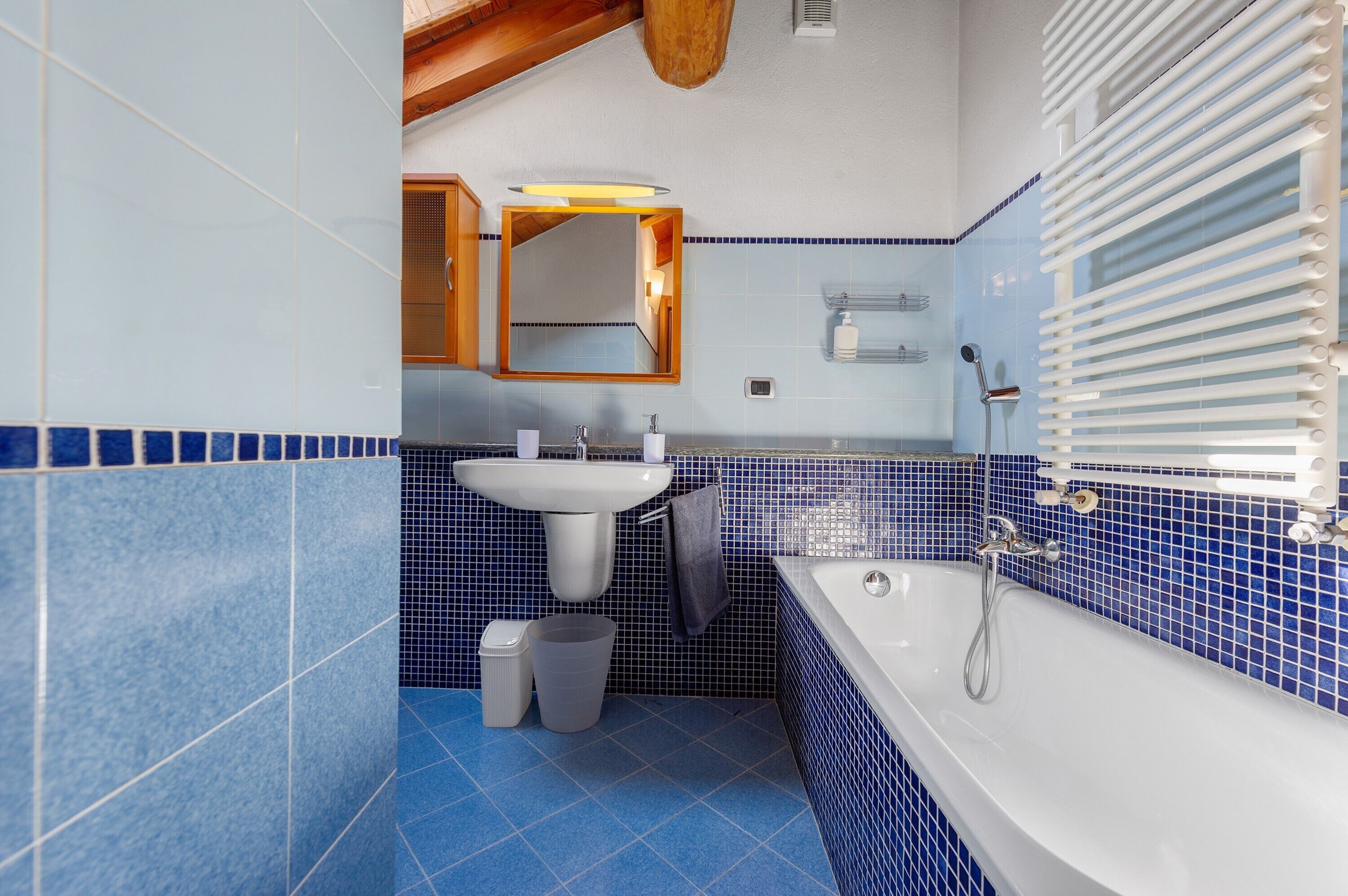 Un baño con lavamanos, espejo y bañera, con azulejos azules.